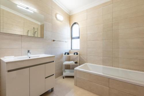 a bathroom with a sink and a tub and a mirror at Vilamoura Escape with Private Pool in Vilamoura