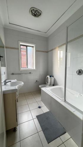 a white bathroom with a tub and a sink at Main road apartment in Sydney