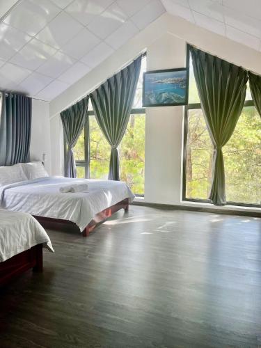 a bedroom with two beds and large windows at Mây Măng Đen Villa in Chương Nghĩa