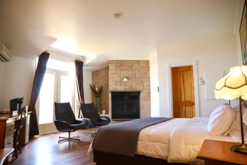 a bedroom with a bed and two chairs and a fireplace at La Remontée Appartements Hôtel in La Malbaie
