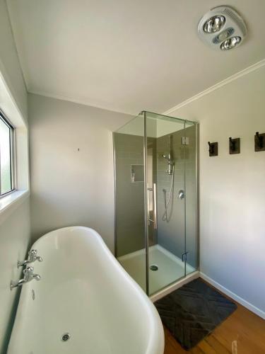 a bathroom with a tub and a glass shower at Cable Bay Moana View House in Cable Bay