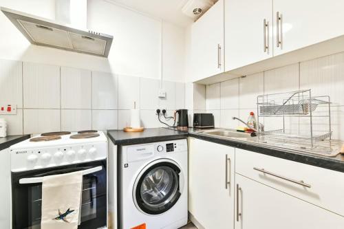 a white kitchen with a washing machine and a sink at Paprika Nest in Hendon
