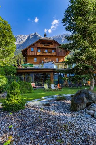 a large wooden house with mountains in the background at Hotel Ramsauhof Zimmer Appartement Pool & Wellness in Ramsau am Dachstein