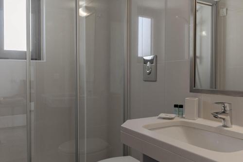 a white bathroom with a shower and a sink at Bella Vista Hotel "by Checkin" in Hersonissos