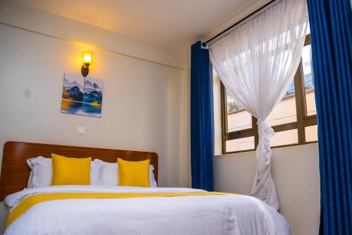 a bedroom with a bed and a window with blue curtains at Sai Inn Eldoret in Eldoret
