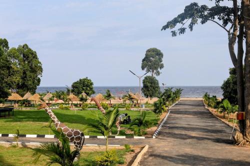 a giraffe walking down a road next to the ocean at Dream Land Resort Beach in Mpigi