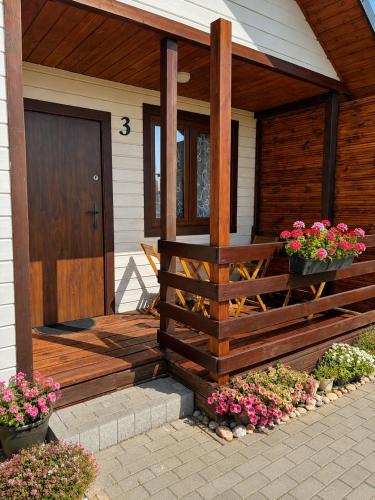 a house with a wooden porch with flowers on it at Domki letniskowe MagNat 700m od morza! in Rusinowo