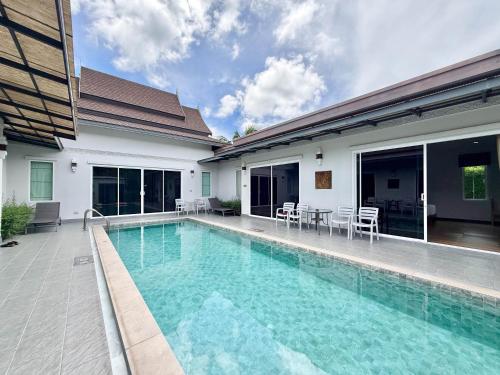 a swimming pool next to a building with chairs and tables at Phuket La Siesta, Naiharn Beach in Nai Harn Beach