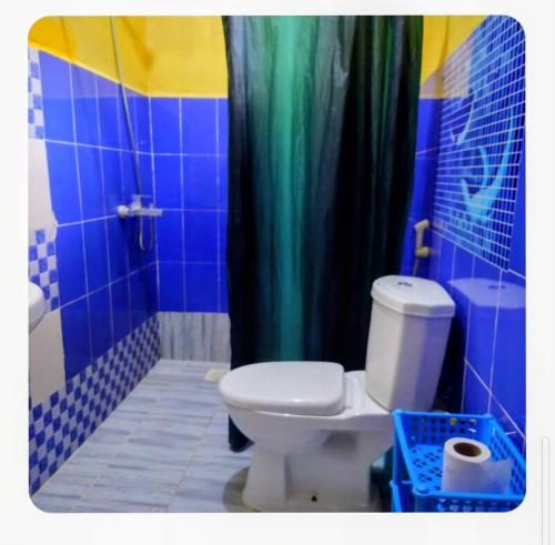 a bathroom with a toilet and a blue shower curtain at Furaha Rena -Kendwa in Kendwa