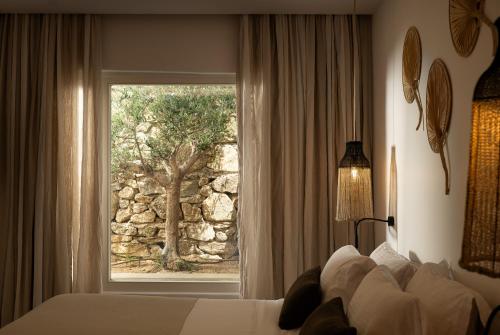 a bedroom with a bed and a window with a tree at Oliving Mykonos Luxury Suites in Klouvas