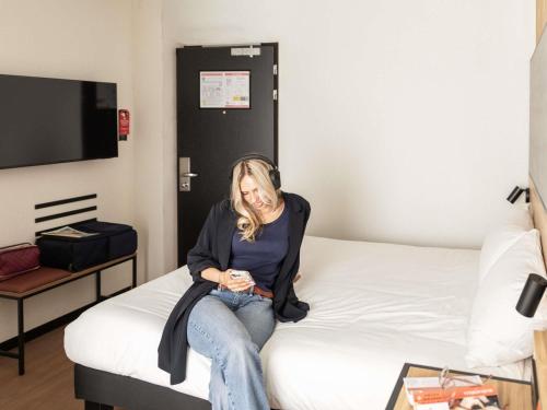 a woman sitting on a bed in a hotel room at ibis Antwerpen Centrum in Antwerp
