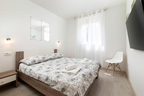 a white bedroom with a bed and a chair at Apartments Jana in Krk