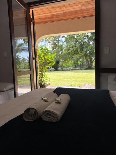a bed with two towels on it with a large window at Pousada Porto do Rio in Caraguatatuba