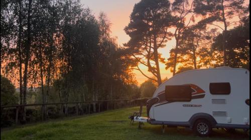 a white trailer parked in a field with the sunset in the background at Woodlands camping in Greatham