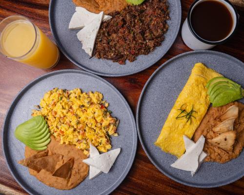 four plates of food on a wooden table with drinks at Hotel Calma Celesti in Perihuete