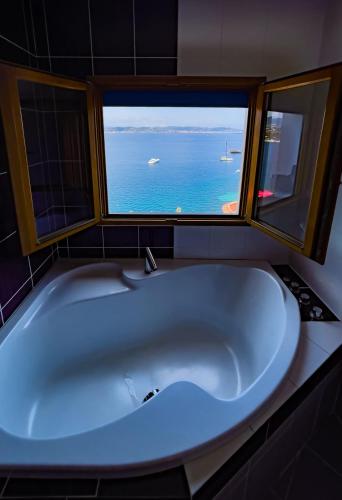 a large tub in a bathroom with two windows at La Coraillère Waterfront Villa with Private Pool and Sea Access in Théoule-sur-Mer