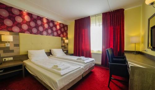 a hotel room with two beds and a desk and a window at Hotel Zwanenburg Amsterdam Airport in Zwanenburg
