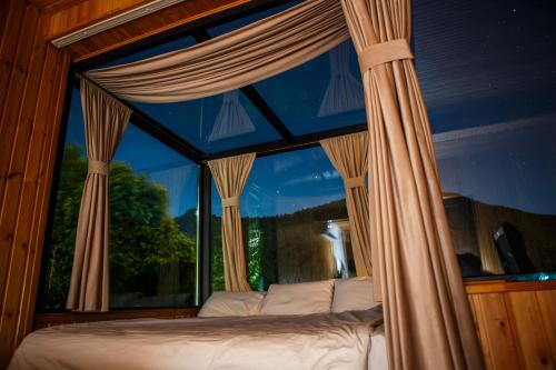a bedroom with a bed in front of a window at Sky Glass Cottage in Kʼveda Chʼkhutunetʼi