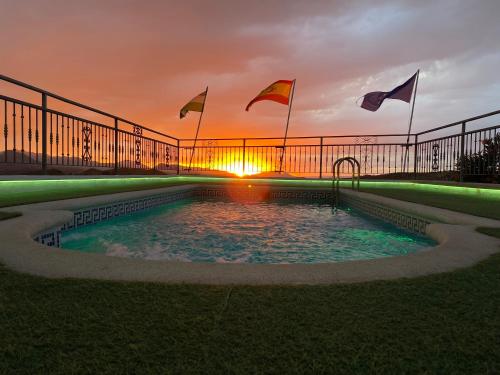 a swimming pool with flags and a sunset in the background at Hotel Sierra de Huesa in Huesa