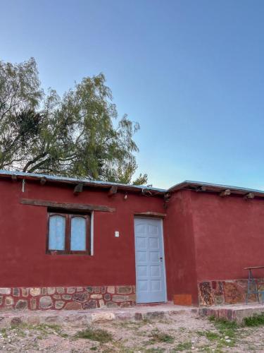 a red house with a white door and a tree at Cabañas tilcara sarahuayco in Tilcara