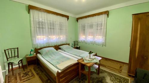 a bedroom with a bed and a table and two windows at Golyafeszek Vendeghaz in Sîncraiu