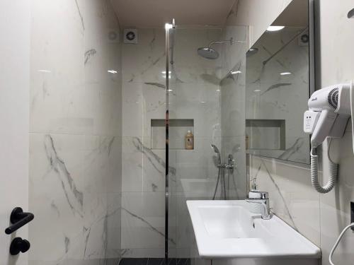 a white bathroom with a shower and a sink at Hotel Djakbe in Tirana