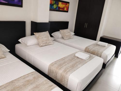 three beds in a room with white sheets and pillows at Hotel Metropolitano in Neiva