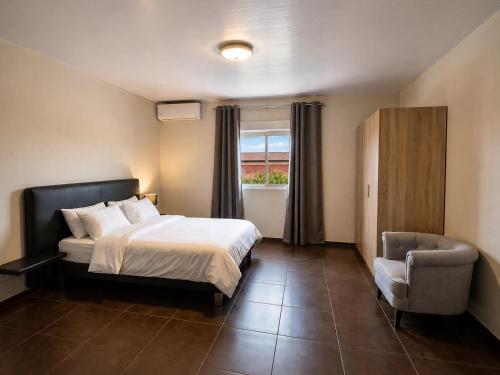 a bedroom with a bed and a chair and a window at L'Eskale Guyane in Montjoly