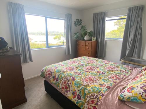 a bedroom with a bed with a colorful bedspread and two windows at Mangōnui Harbour Haven in Mangonui