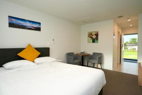 a bedroom with a white bed and a table with chairs at Yates Park Motel in Auckland