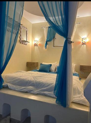 a bedroom with a bed with blue curtains at Dar Ahlem Djerba in El Guecheïne
