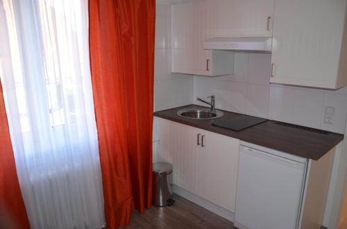 une petite cuisine avec un évier et un rideau orange dans l'établissement Hotel Restaurant Kniebishöhe, à Freudenstadt