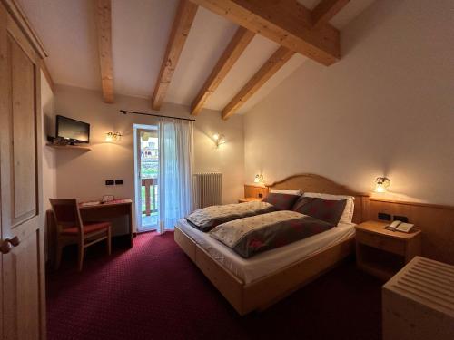 a bedroom with a bed and a table and a window at Hotel Vigo in Vigo di Fassa