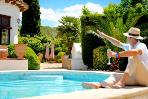a man in a hat sitting next to a swimming pool at Mas Boronat Resort in Salomó