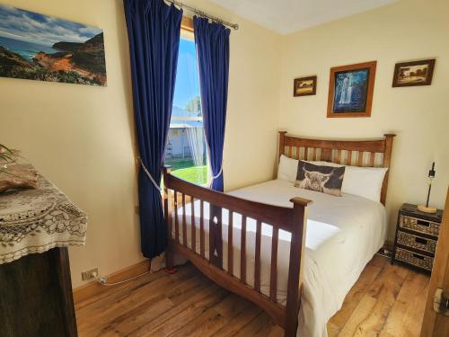 a bedroom with a bed and a window with blue curtains at Ruby's Cottage Farm Stay in Port Arthur