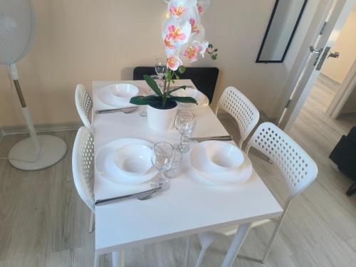 a white table with white plates and glasses and a plant at Yunus in Croydon