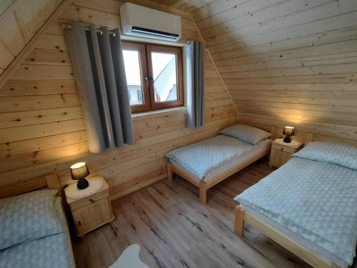 two beds in a log cabin with a window at Domki Pod Lasem Podhale in Zakopane