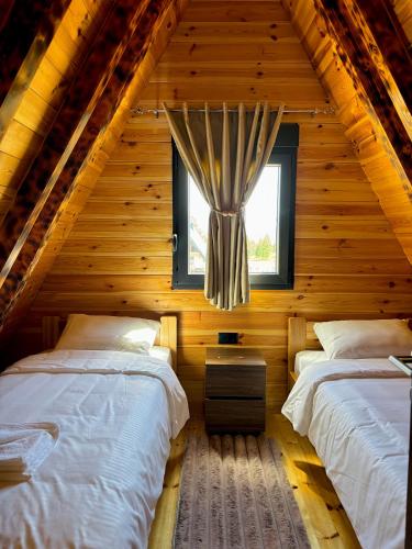 two beds in a log cabin with a window at Ðedovina mountain cabins in Žabljak