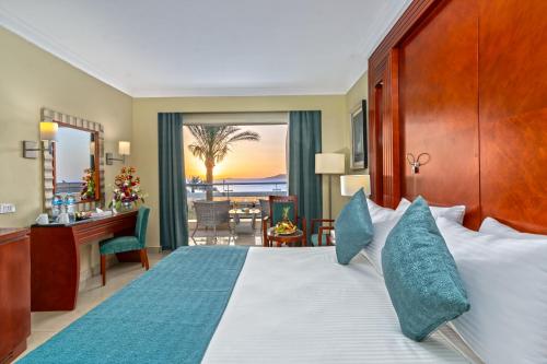 a hotel room with a bed with a desk and a balcony at Xperience Sea Breeze Resort in Sharm El Sheikh