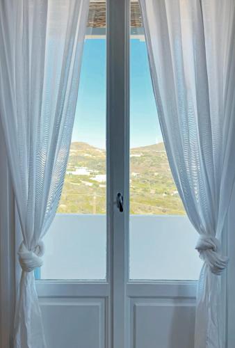 a window with white curtains in a room at Oliaros Seaside Lodge in Agios Georgios