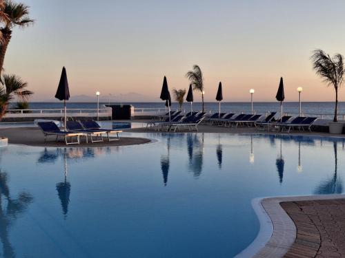 a swimming pool with chairs and the ocean in the background at Villaggio Hotel Agrumeto in Capo Vaticano