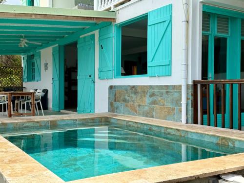 a swimming pool with blue shutters on a house at Espace Harmonie Deshaies - Vue Mer & Piscine Panoramique in Deshaies
