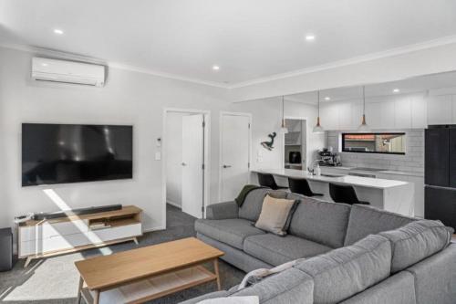 a living room with a gray couch and a kitchen at Recline on Leo in Waihi Beach