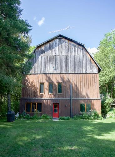 a large wooden barn with a red door at The Barn - A Unique Gathering Place in Sainte-Cécile-de-Masham