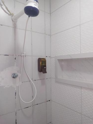 a shower head in a white tiled bathroom at Fênix hospedaria in Natal