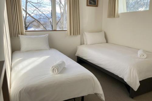 two beds in a room with white sheets and a window at Chalet Tsugaike in Otari