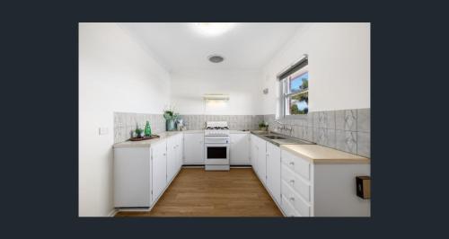 a white kitchen with white cabinets and a window at Seaside Adelaide Holiday Apartment 2BR 1 min walk to Brighton Beach in Adelaide