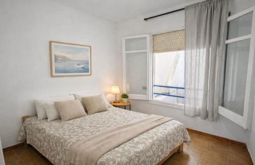 a white bedroom with a bed and a window at La Casa de la Punta in San Pol de Mar