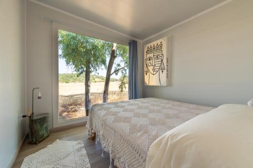 a bedroom with a bed and a large window at Macondo Agriliving Tiny Houses in Castiadas