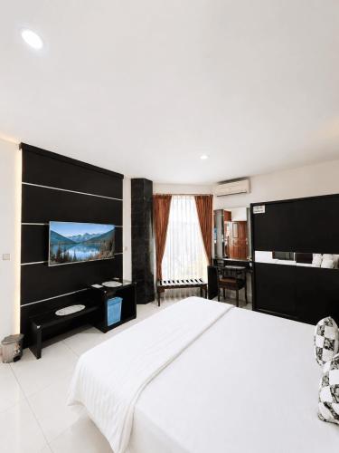 a bedroom with a white bed and a flat screen tv at Enny's Guest House in Malang